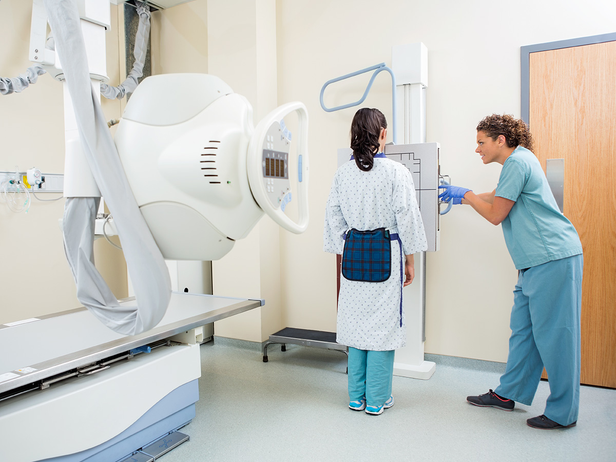 1200x900GMB-3 A nurse adjusting an x-ray machine for a female patient in the examination room.
