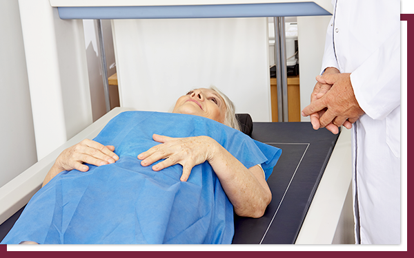 IMG 3 A woman laying on a DEXA scan table in a hospital gown with a doctor standing next to her.