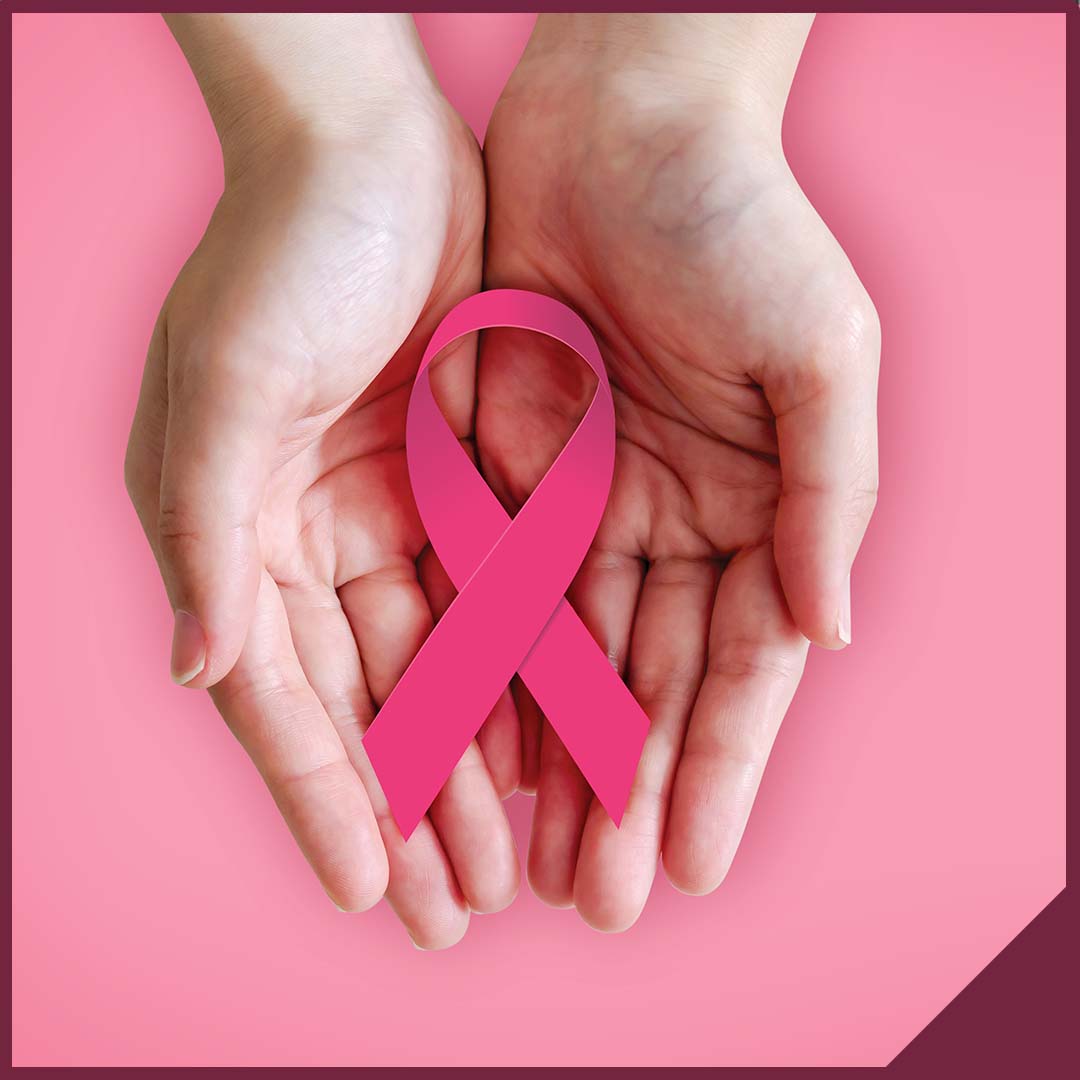 Hands holding a pink ribbon for breast cancer with a pink background beneath them.