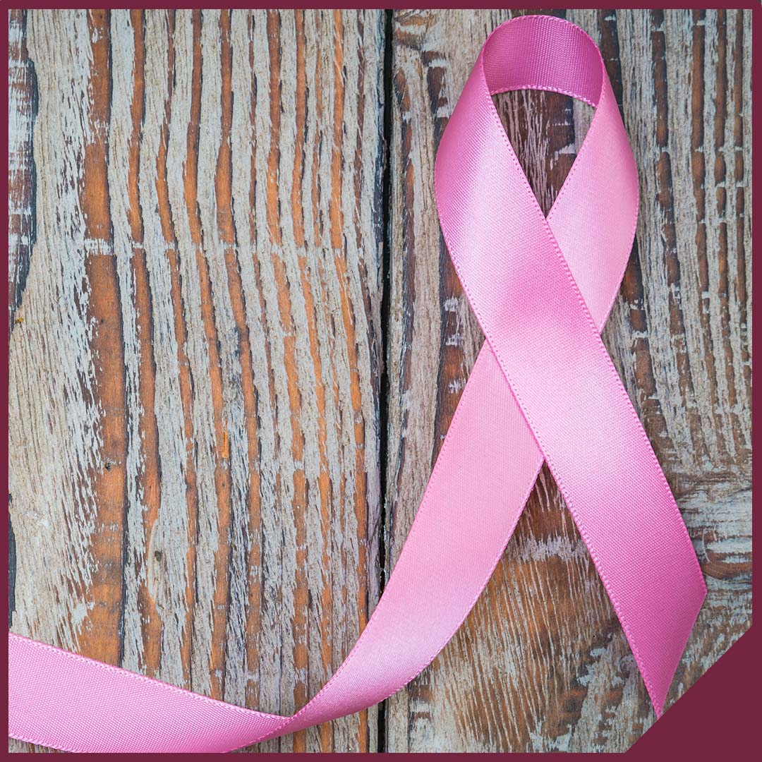 Image-2 A pink breast cancer awareness ribbon sitting on a wood background.