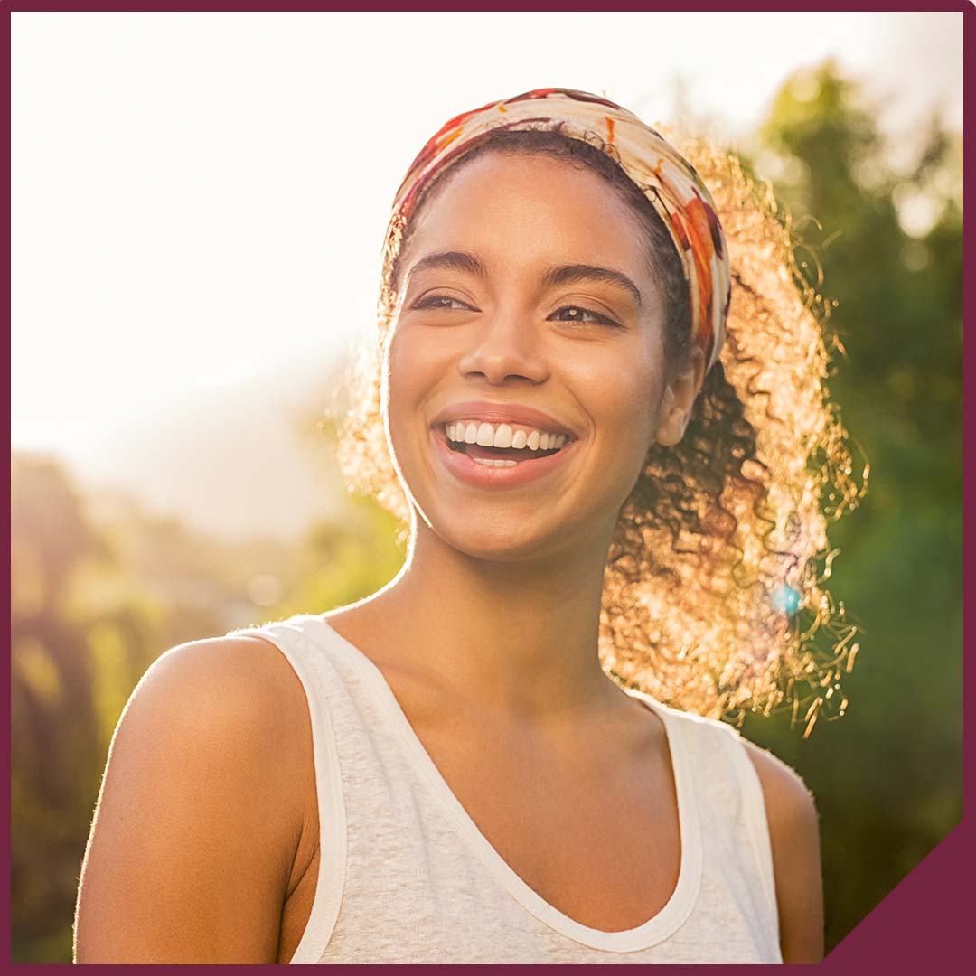 Image-4 Portrait of a smiling young woman with the sun shining behind her.