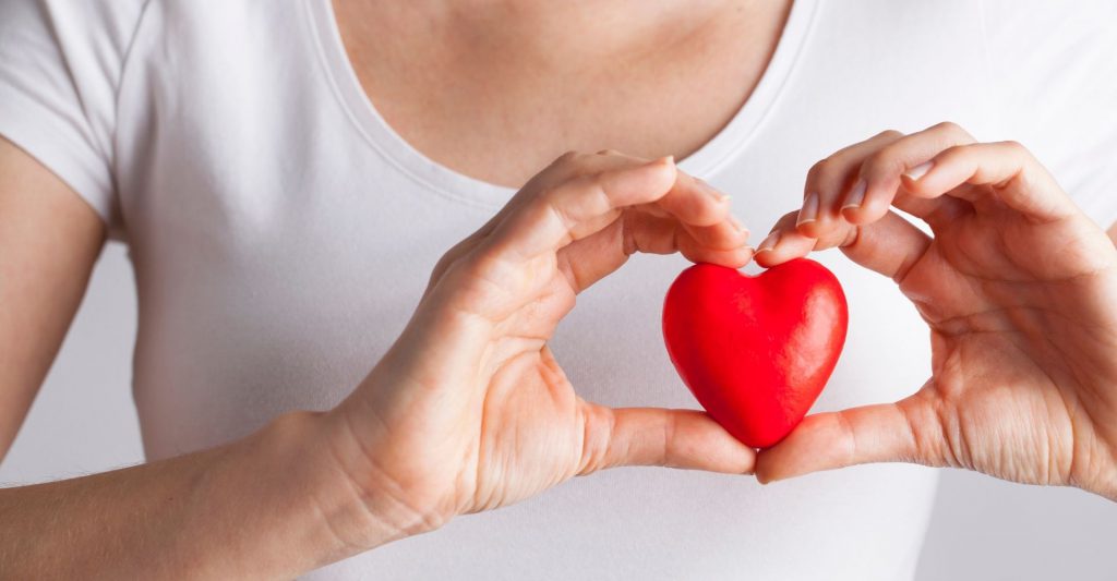 An image of a woman holding a toy heart over her chest.